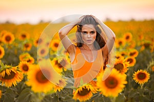 Beautiful young girl enjoying nature on the field of sunflowers at sunset. Summertime. Attractive brunette woman with long healthy