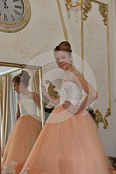 Beautiful young girl with evening haircut in pink with white a  lash by a gilded mirror, fitting