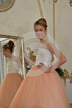 Beautiful young girl with evening haircut in pink with white a  lash by a gilded mirror, fitting