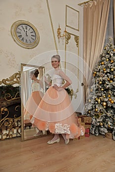 Beautiful young girl with evening haircut in pink with white a  lash by a gilded mirror, fitting