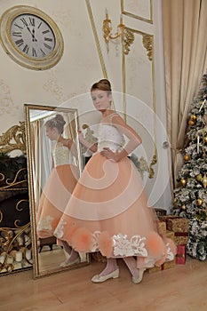 Beautiful young girl with evening haircut in pink with white a  lash by a gilded mirror, fitting