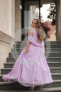 Beautiful young girl in evening lavender dress stand in stairs by restaurant