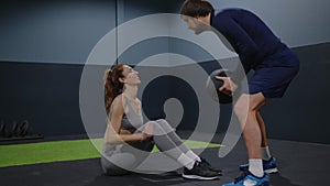 Beautiful young girl exercises with personal trainer, doing sit-ups with black ball, throwing pass back and forth. Fit