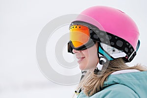 A beautiful young girl in an extreme sports suit, a hat and a helmet with a mask on the winter slope is holding alpine