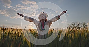 Beautiful young girl with flower chaplet, ethnic folklore dress with traditional Bulgarian embroidery during sunset on wheat field