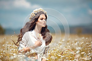Beautiful young girl with flower enjoying in chamomile field. Carefree happy brunette woman with chaplet on healthy wavy hair