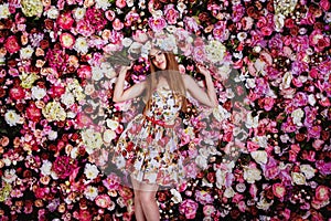 A beautiful young girl with flowers bouquet near a floral wall.