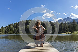 Beautiful young girl and former woman plays her cello on a wooden jetty