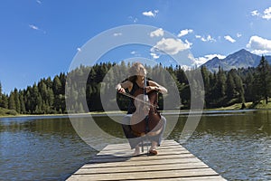 Beautiful young girl and former woman plays her cello on a wooden jetty