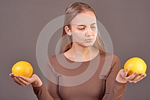 Beautiful young girl in a good mood posing on a gray background with two oranges