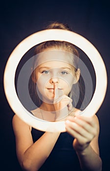 Beautiful young girl gymnast holding a glowing circle and making quiet gesture
