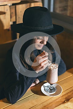 Beautiful young girl in hat drinking coffee in cafe