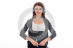 Beautiful young girl in headphones and gray jacket looks into the camera and smiles holding Tablet