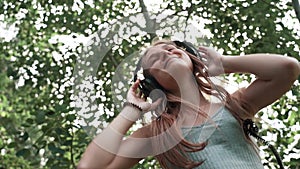 Beautiful, young girl with headphones in nature listening to music and dancing to the beat, close-up, slow motion