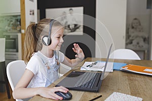 Beautiful young girl with headset is sitting in front of her laptop during corona time and is having video call