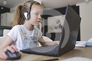 Beautiful young girl with headset is sitting in front of her laptop during corona time and is having video call