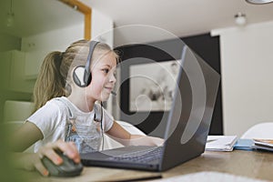 Beautiful young girl with headset is sitting in front of her laptop during corona time and is having video call