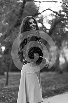 Beautiful young girl in a heavy leather jacket, with long beautiful black hair posing on the background in the park