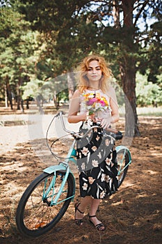 Beautiful young girl with her bike cruiser and flowers on autumn field. The best time to walk with a bicycle.