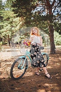 Beautiful young girl with her bike cruiser and flowers on autumn field. The best time to walk with a bicycle.