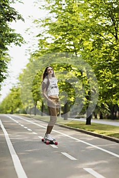 Beautiful young girl hipster T-shirt, shorts and sneakers rides on the track in park on a longboard. Skateboarding. lifestyle