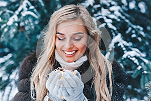 Beautiful young girl holdinf christmas lights in her hands in winter forest