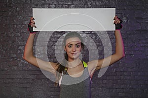 Beautiful young girl holding an empty board, copy space for advertising, muscles and gym, conceptual photo, advertising space