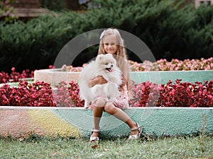 Beautiful young girl holding a funny fluffy dog. A child having fun on a blurred natural background. Happiness concept.