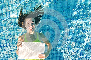 Beautiful young girl holding white blank board in swimming pool under water, fitness and underwater fun