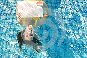 Beautiful young girl holding white blank board in swimming pool under water, fitness and underwater fun