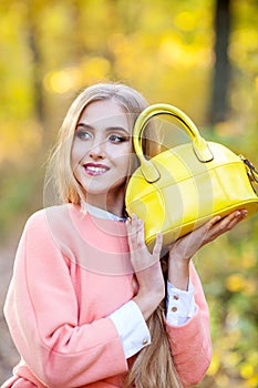 Beautiful young woman with yellow fashionable bag in hands on autumn nature