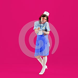 Beautiful young girl in image of retro cater waiter wearing 70s, 80s fashion style uniform isolated over bright pink