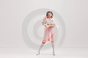 Beautiful young girl in image of retro cater waiter wearing 70s, 80s fashion style uniform isolated over light studio