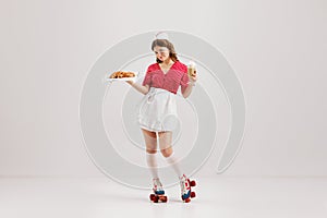 Beautiful young girl in image of retro cater waiter wearing 70s, 80s fashion style uniform isolated over light studio