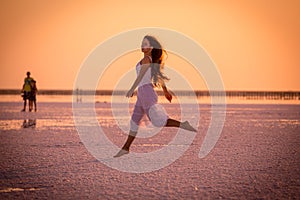 Beautiful young girl jumping on the salt lake at sunset