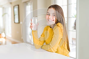 Beautiful young girl kid drinking a fresh glass of water with a happy face standing and smiling with a confident smile showing