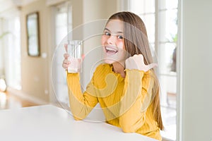 Beautiful young girl kid drinking a fresh glass of water pointing and showing with thumb up to the side with happy face smiling