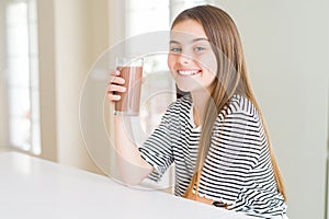 Beautiful young girl kid drinking fresh tasty chocolate milkshake as snack with a happy face standing and smiling with a confident