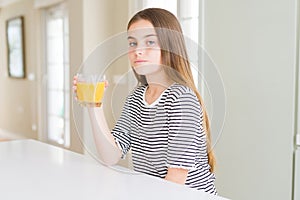 Beautiful young girl kid drinking a glass of fresh orange juice with a confident expression on smart face thinking serious