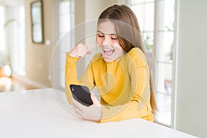 Beautiful young girl kid sending a message using smartphone screaming proud and celebrating victory and success very excited,