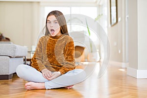 Beautiful young girl kid sitting on the floor at home afraid and shocked with surprise expression, fear and excited face