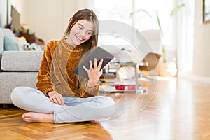 Beautiful young girl kid using digital touchpad tablet sitting on the floor with a happy face standing and smiling with a