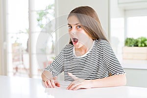 Beautiful young girl kid wearing stripes t-shirt afraid and shocked with surprise expression, fear and excited face