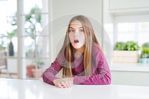 Beautiful young girl kid on white table afraid and shocked with surprise expression, fear and excited face