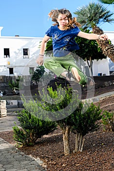 Beautiful young girl leaping over plants in a garden