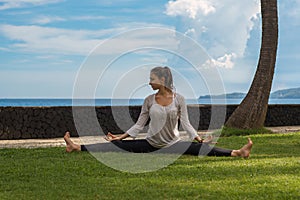 Beautiful young girl in leggings and tunic makes yoga practice, meditation on the ocean beach in Bali Indonesia