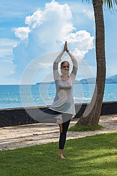 Beautiful young girl in leggings and tunic makes yoga practice, meditation on the ocean beach Bali Indonesia