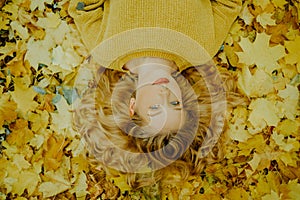 A beautiful young girl lies in the park with autumn leaves, a cute model with beautiful blond hair. Autumn discounts, autumn