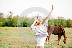 A beautiful young girl, with light curly hair in a straw hat near horses, in the countryside, warm autumn
