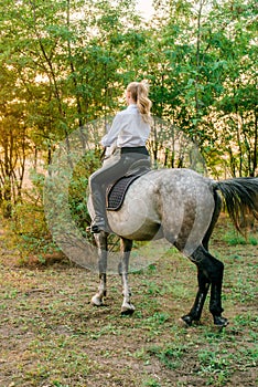 Beautiful young girl with light hair in uniform competition smiling and astride a horse in sunset